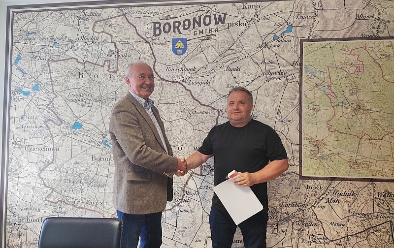 Mężczyźni podają sobie rękę na potwierdzenie podpisania umowy, w tle na ścianie mapa Gminy Boronów.