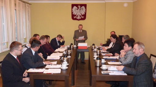 Pierwsza sesja VII kadencji Rady Gminy w&nbsp;Boronowie. Radni siedzą przy stołach w&nbsp;sali obrad, a&nbsp;stojący mężczyzna odczytuje dokument.