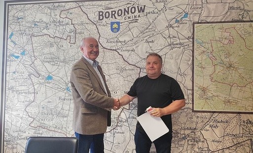 Mężczyźni podają sobie rękę na potwierdzenie podpisania umowy, w tle na ścianie mapa Gminy Boronów.
